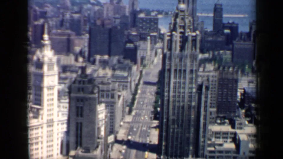 High-angle 1958 view of downtown Chicago, showing clustered skyscrapers, a straight street below, rooftops, and the soft color texture of 8mm film.