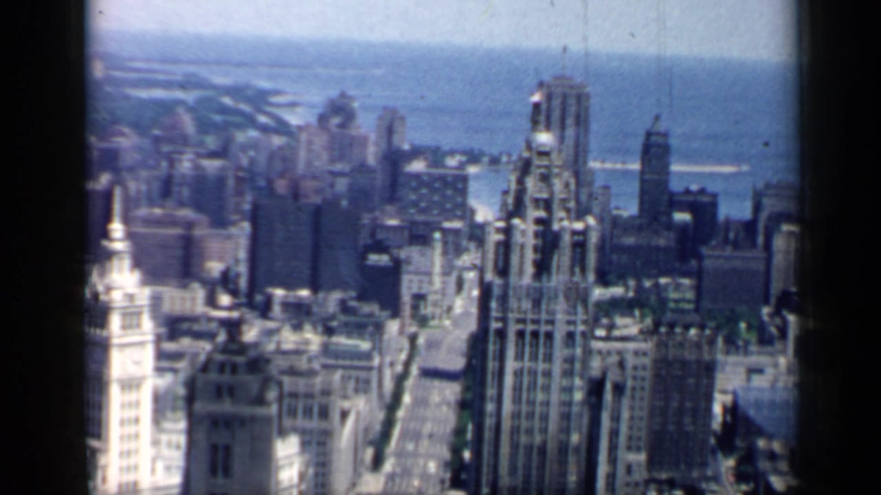 Aerial or elevated 1958 view of downtown Chicago, showing towers, city blocks, and Lake Michigan through a soft vintage 8mm frame.