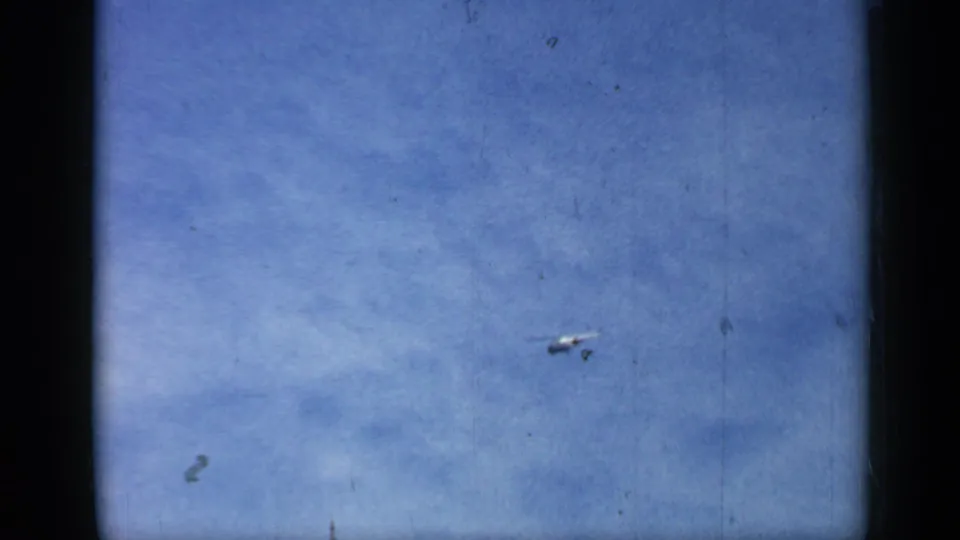 Small aircraft or helicopter in flight against a blue Chicago sky, captured on grainy 1958 8mm home-movie film.