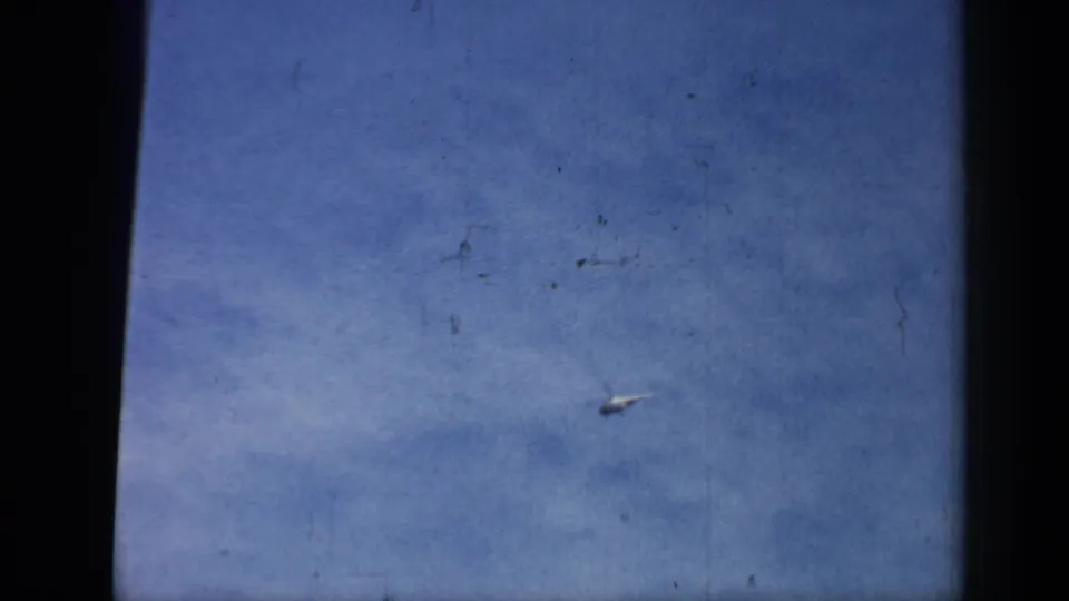 Small aircraft or helicopter continues across an open blue sky in the Chicago 1958 home-movie clip, with dust and scratches visible.
