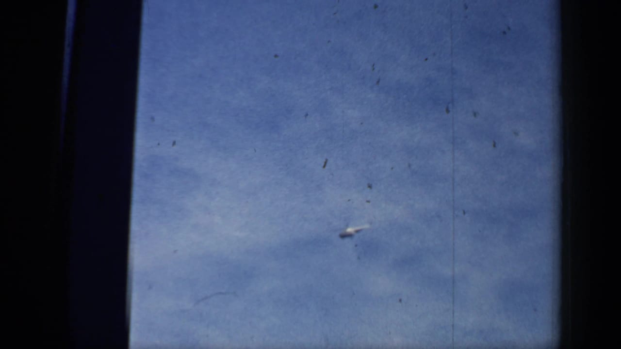 Distant helicopter flying across a blue sky with dark film frame edges.