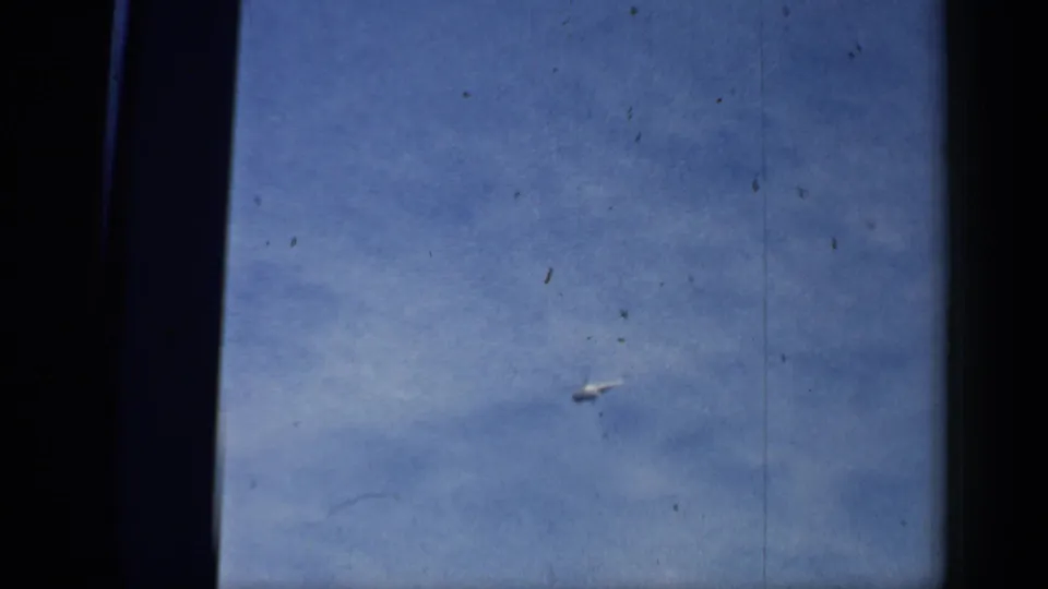 A small helicopter crosses a blue sky in 1958 Chicago home-movie footage, framed by dark 8mm film borders and visible dust specks.