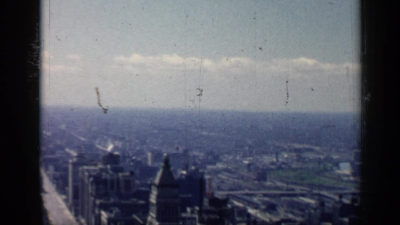 Hazy city skyline seen from above with tall buildings and distant horizon.