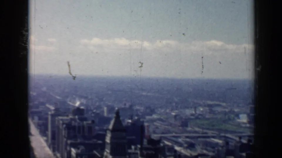 High vantage view over Chicago in 1958, with hazy downtown buildings, a broad horizon, and dark 8mm frame edges.