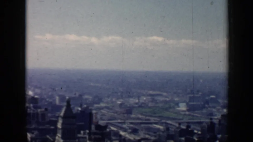 A soft 1958 Chicago city view from above, showing downtown rooflines, a green open area, and hazy distance through an 8mm frame.