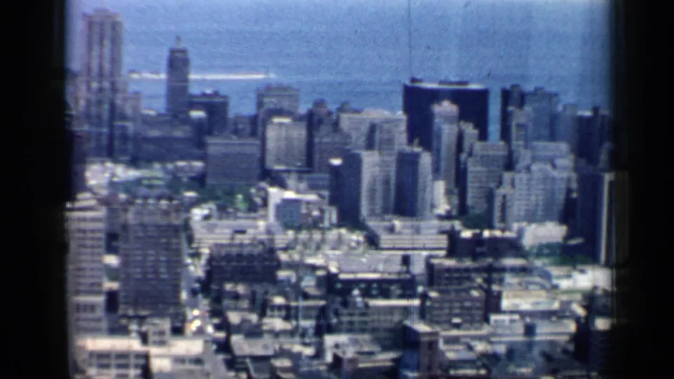 1958 Chicago aerial pan across dense downtown blocks, towers, and a distant Lake Michigan horizon.