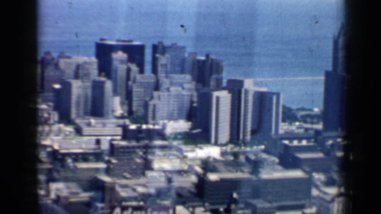 1958 Chicago skyline with clustered high-rises and Lake Michigan in the background, framed by dark 8mm gate edges.