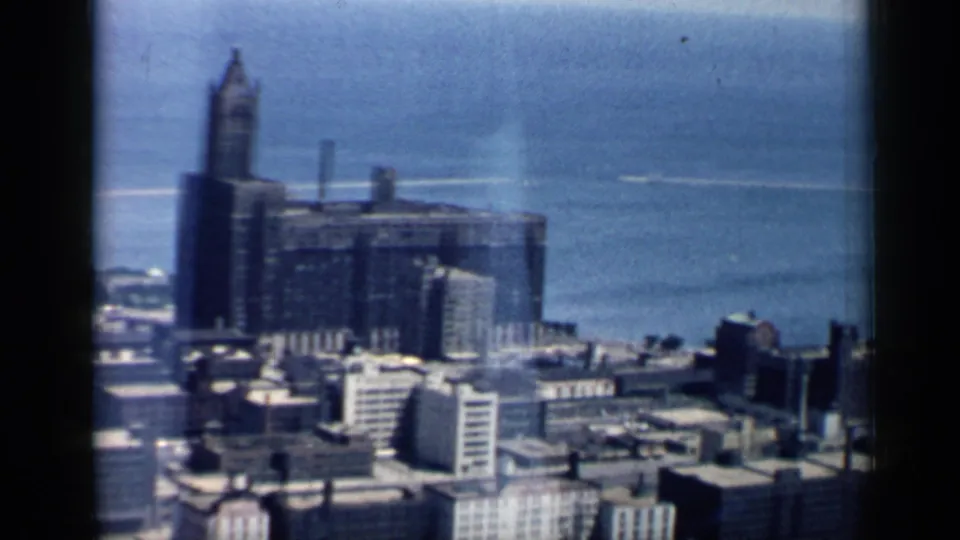Late-1950s Chicago skyline segment with Lake Michigan, shoreline structures, and soft blue 8mm film texture.