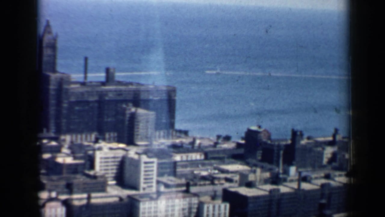 Elevated view of Chicago buildings beside blue lake water, framed by dark film borders.