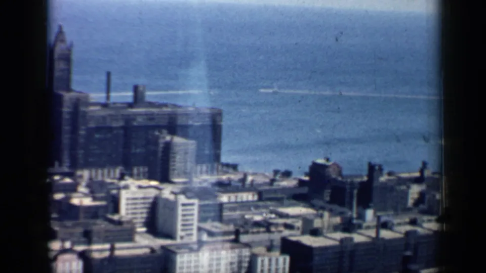 1958 8mm frame showing an elevated Chicago lakefront view with downtown buildings, rooftops, and Lake Michigan beyond.