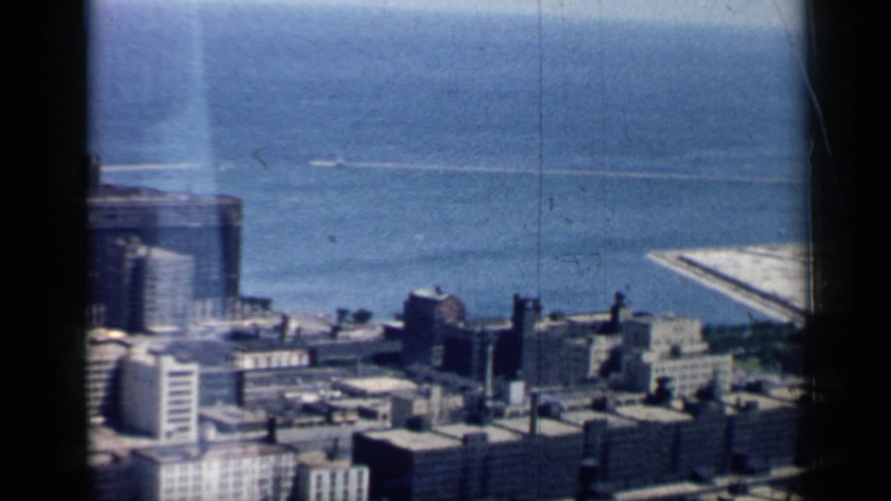 City rooftops and lakefront water with a bright shoreline structure at the right edge.