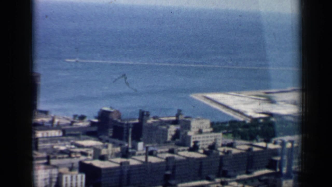 Elevated 1958 Chicago lakefront view showing clustered buildings, blue water, and a pale pier or breakwater along the shoreline.