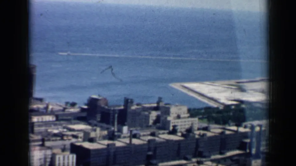 Elevated 1958 Chicago lakefront view showing clustered buildings, blue water, and a pale pier or breakwater along the shoreline.