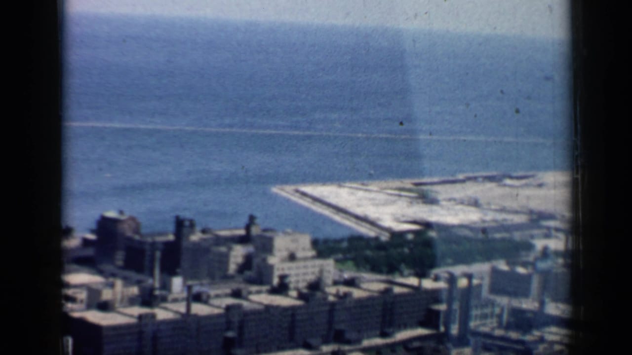 Final 1958 8mm frame of Chicago from above, with downtown rooftops below and Lake Michigan and shoreline structure in the background.