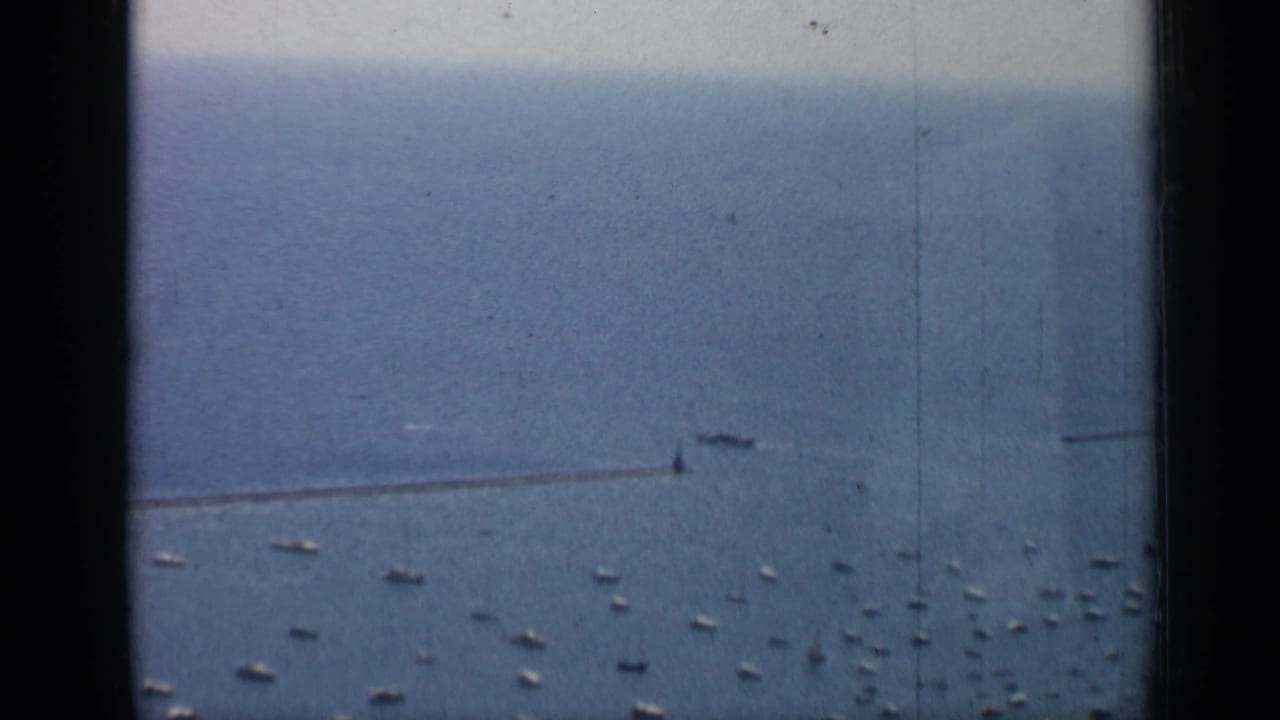 Lake water with a long breakwater and many small boats seen from a high vantage point.