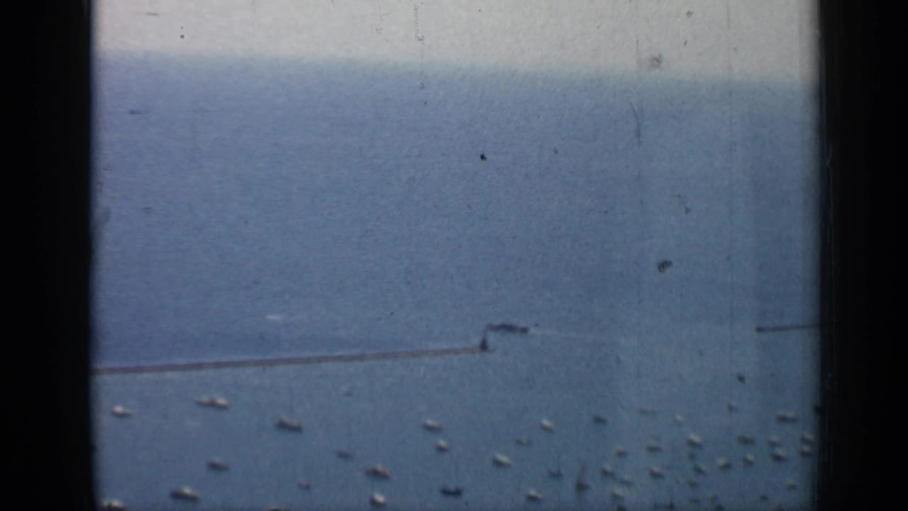 Chicago lakefront frame from 1958 showing scattered boats on blue water beside a long breakwater, with soft grain and edge shadows.