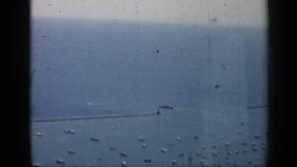 Chicago lakefront frame from 1958 showing scattered boats on blue water beside a long breakwater, with soft grain and edge shadows.