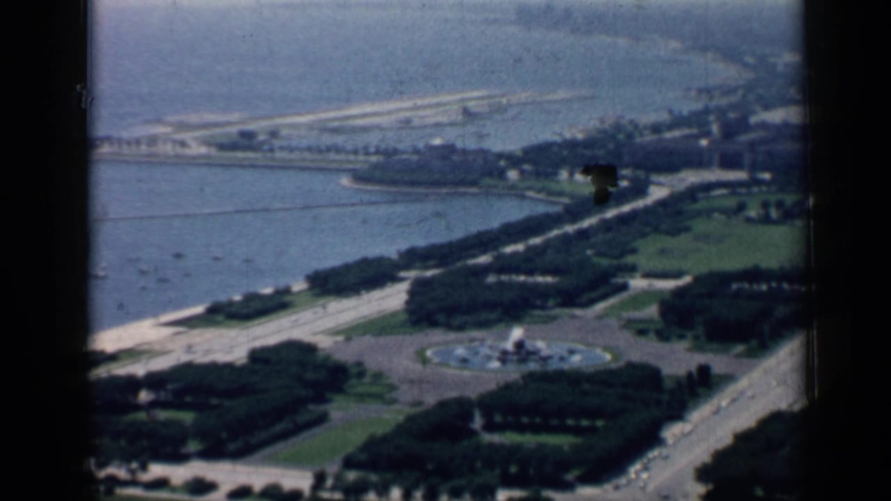 1958 Chicago aerial view of lakefront park areas with roads, trees, a circular fountain, shoreline water, and boats beyond.