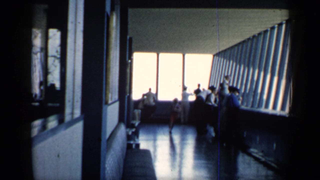1958 Chicago 8mm frame inside a public observation-like interior, where visitors stand near large windows in silhouette.