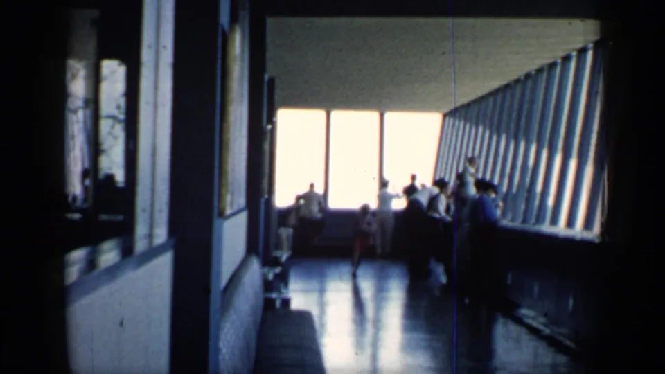 1958 Chicago 8mm frame inside a public observation-like interior, where visitors stand near large windows in silhouette.