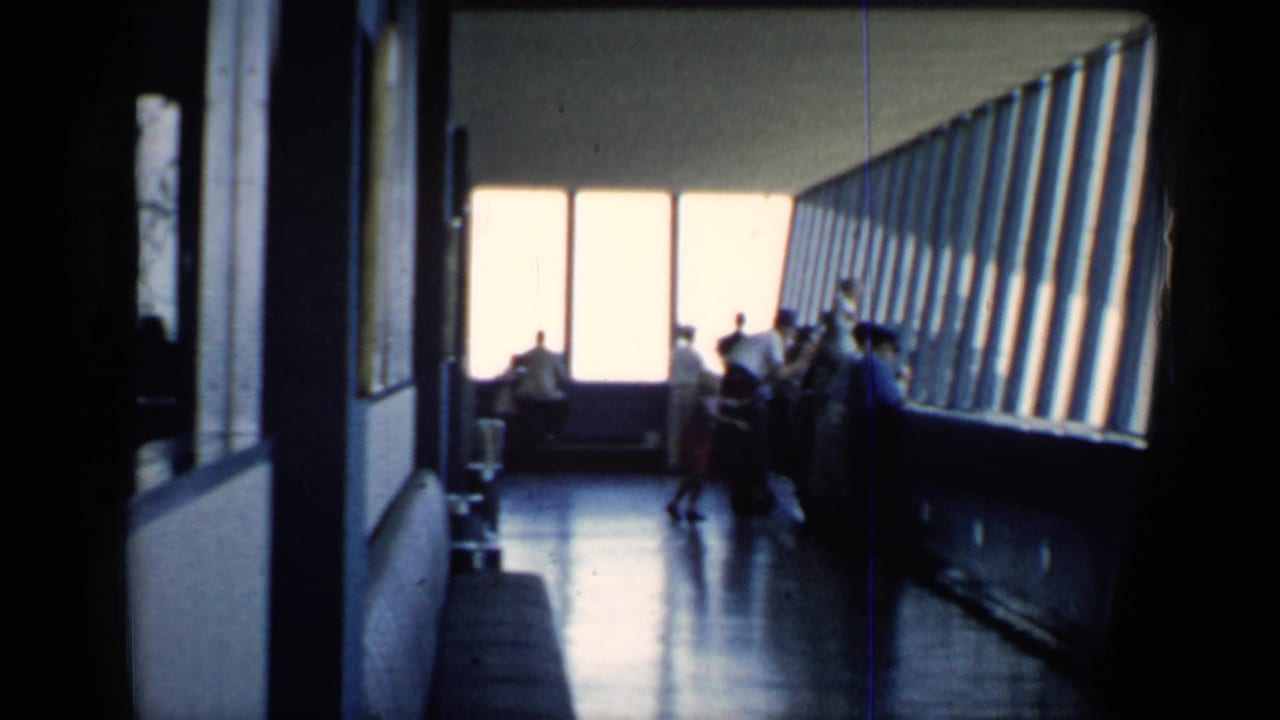 1958 Chicago home-movie frame showing visitors silhouetted in a windowed indoor viewing area at a public attraction.
