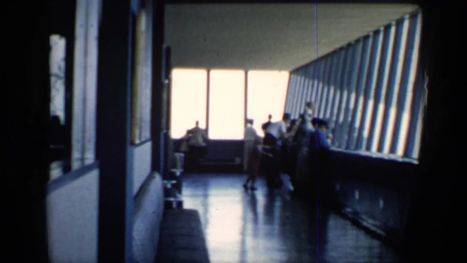 1958 Chicago home-movie frame showing visitors silhouetted in a windowed indoor viewing area at a public attraction.