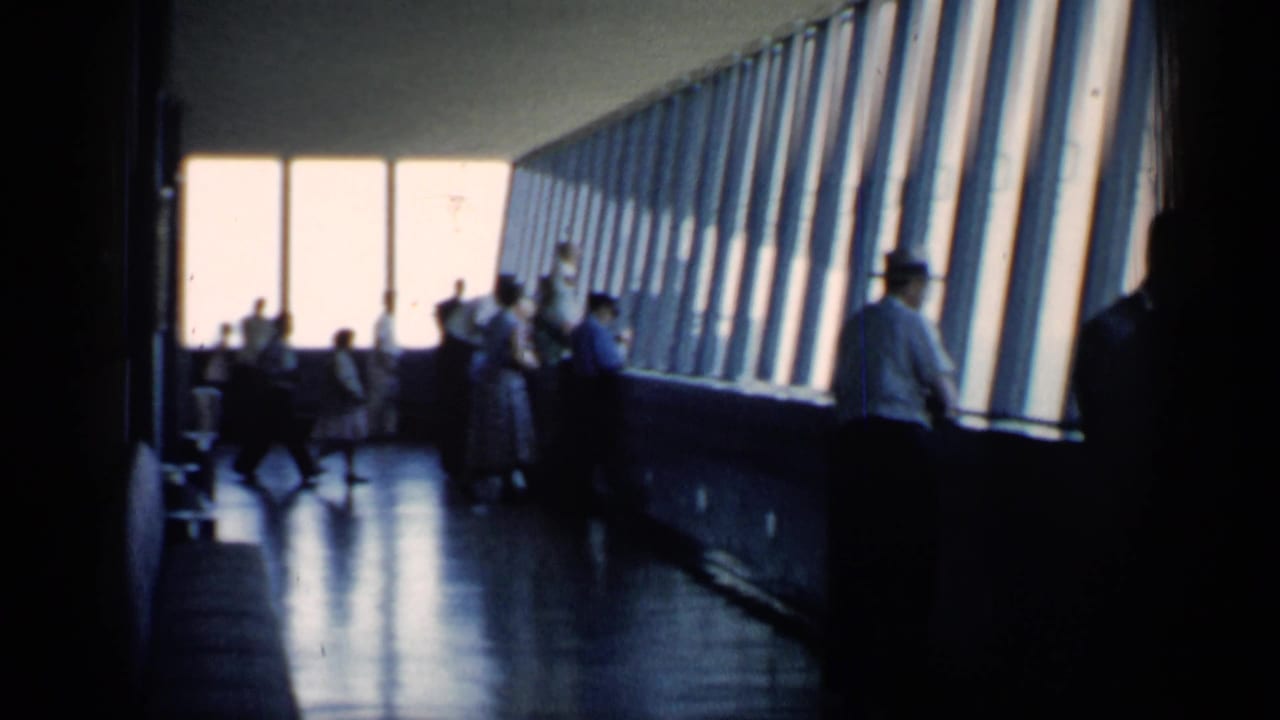 Backlit 1958 Chicago home-movie view of adults and children near large windows in an indoor observation area.