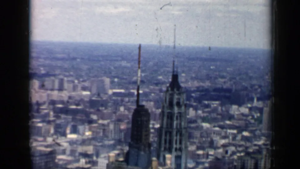 1958 Chicago home-movie frame showing a hazy elevated city panorama with tall towers, antenna masts, and dark 8mm frame edges.