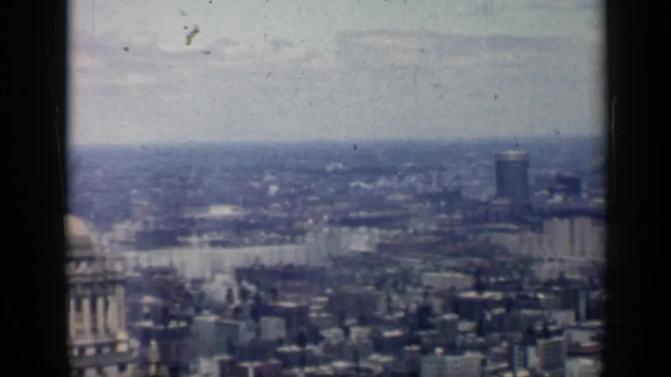 1958 Chicago frame showing a broad skyline from above, with dense buildings, a tall distant tower, and visible film grain.