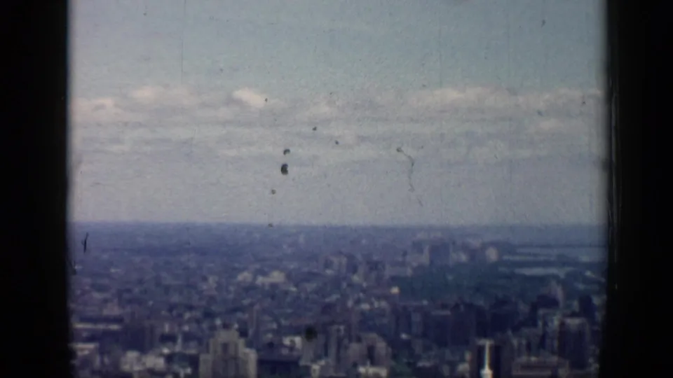 High view over Chicago in 1958, divided by a dark window frame with dense buildings fading into haze.
