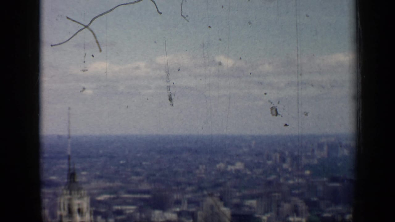 Late-frame 1958 Chicago skyline view with distant buildings, cloudy sky, dark side framing, and surface marks from the film.