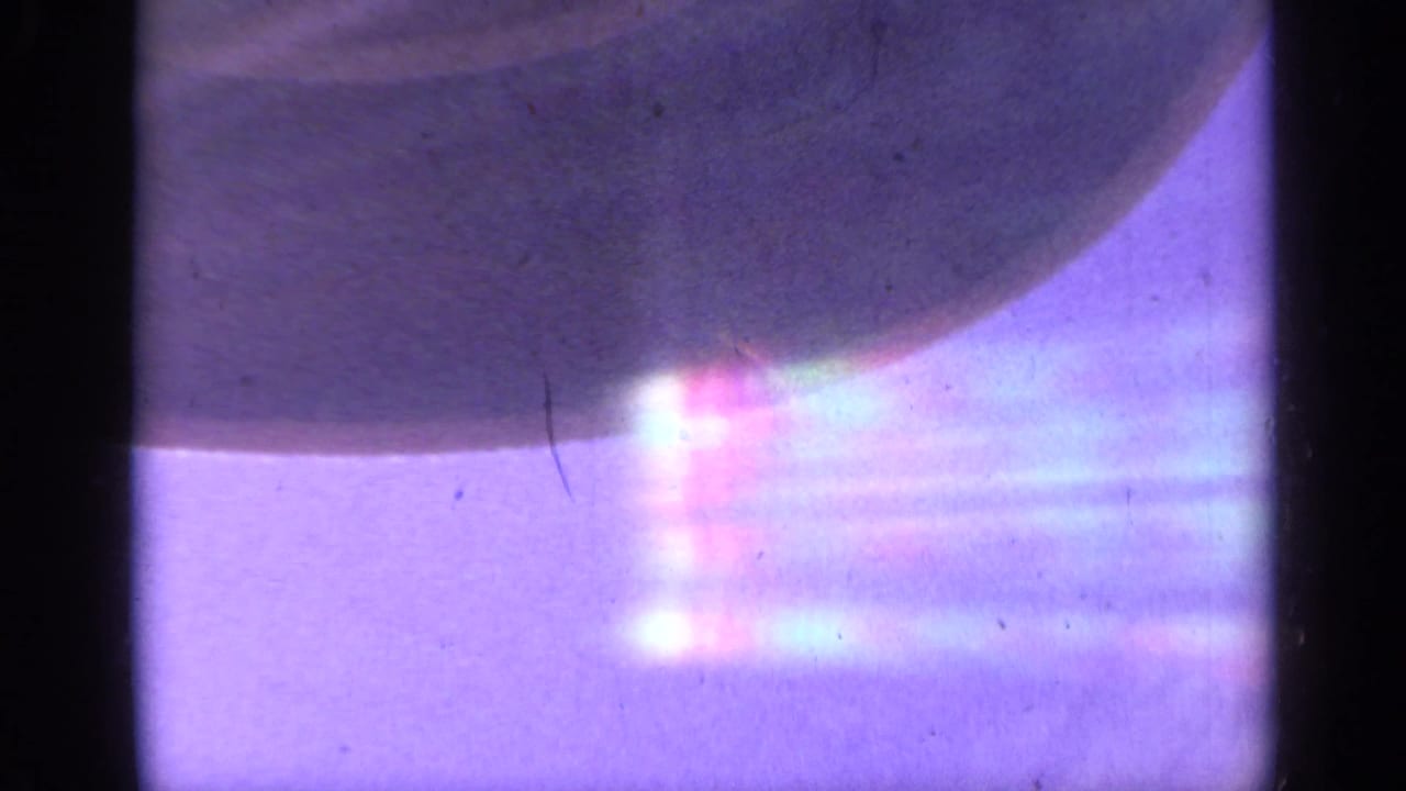 1959 Colorado 8mm frame with a shadowed chairlift-like form crossing a bright, flare-filled blue-purple sky.