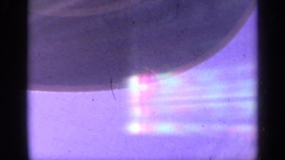 1959 Colorado 8mm frame with a shadowed chairlift-like form crossing a bright, flare-filled blue-purple sky.