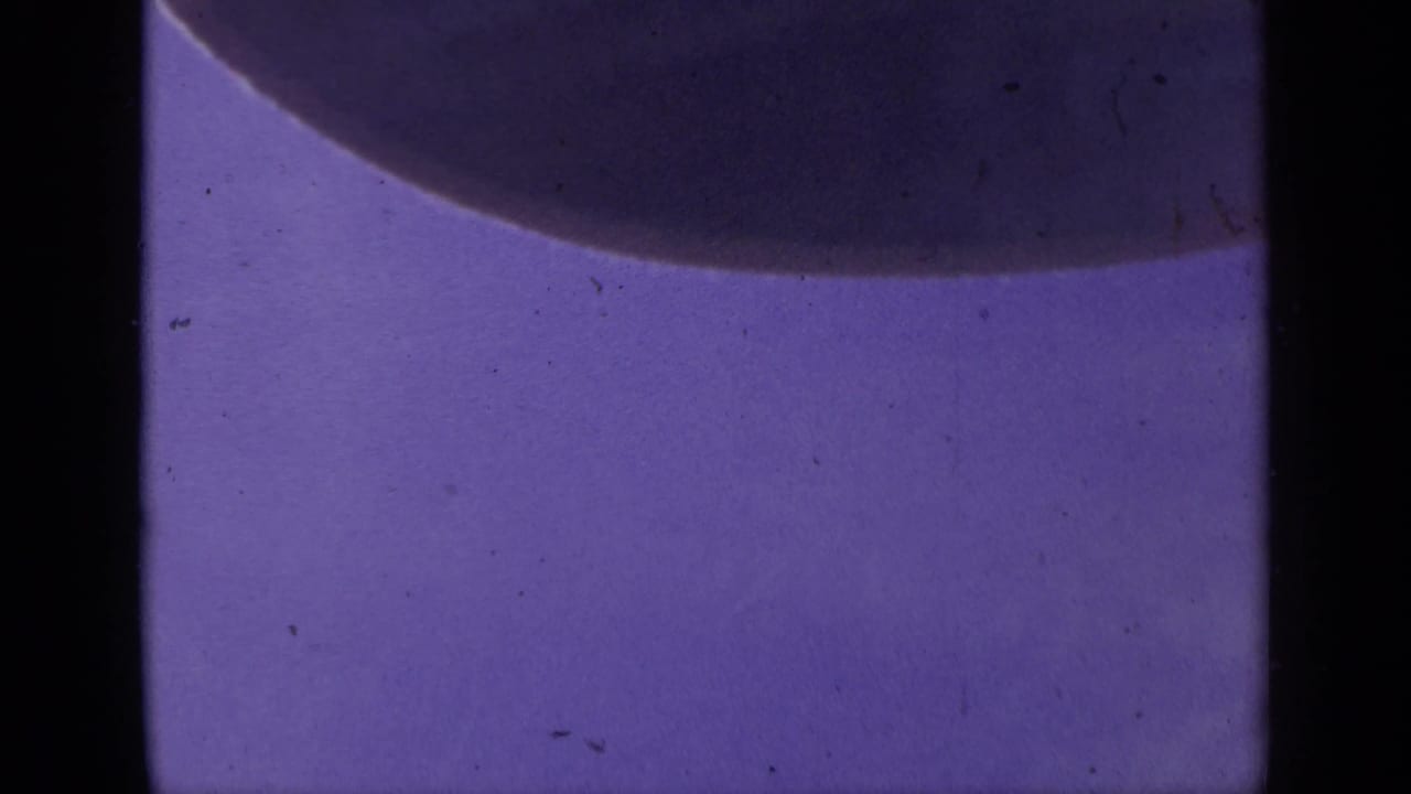 1959 Colorado 8mm frame showing a purple microscope field, a broad dark rounded form, and pronounced small-gauge film borders.