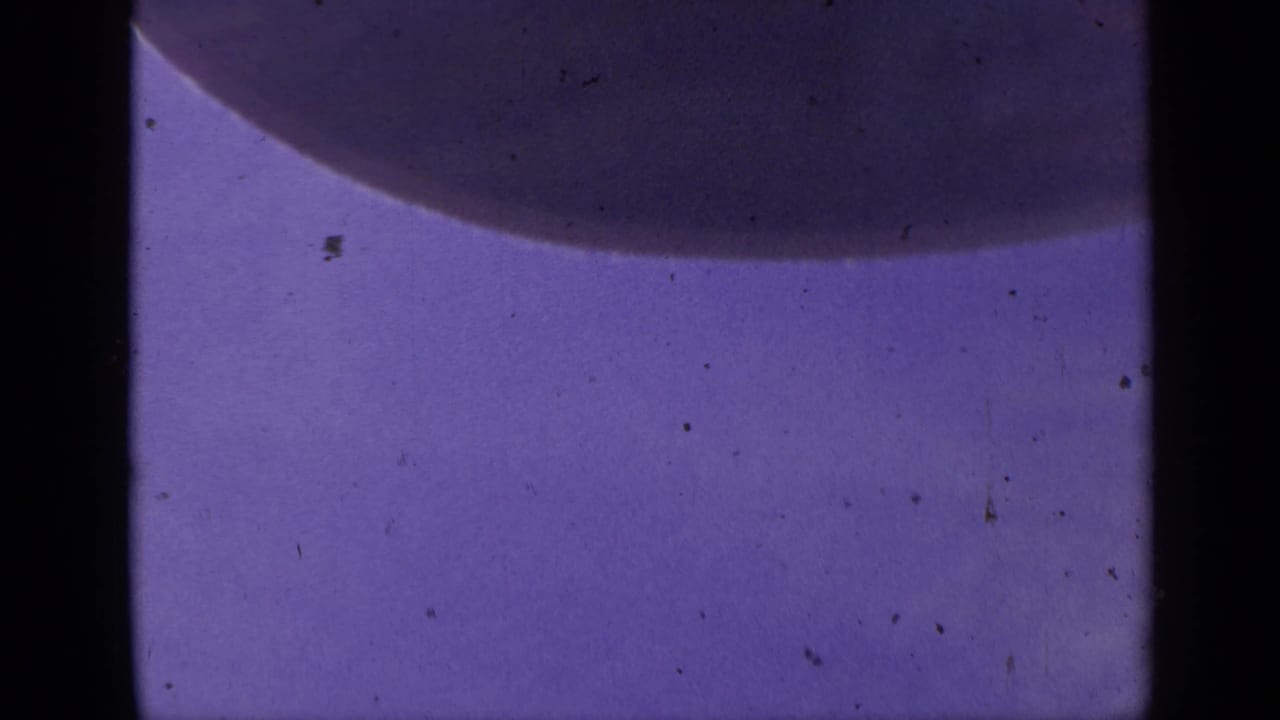 1959 Colorado 8mm microscope frame with a dark rounded cell-like edge against a purple-blue field and visible film wear.