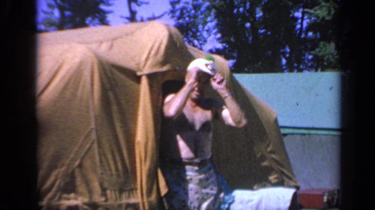 Shirtless man in a white cap adjusts his headwear beside a brown canvas tent.