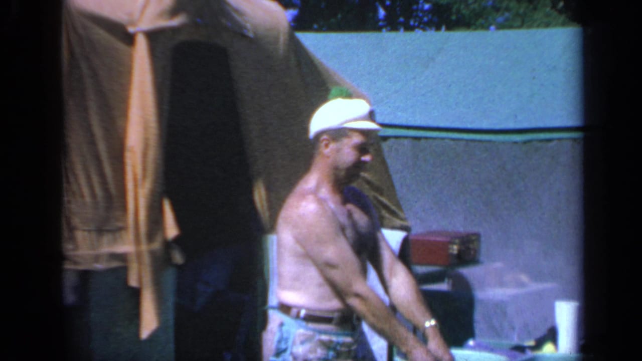 1959 Colorado 8mm frame showing a shirtless man in a white cap near a tent and campsite supplies.