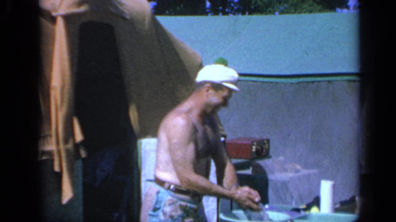1959 Colorado home-movie frame of a man working with food or supplies beside a tent at a campsite.