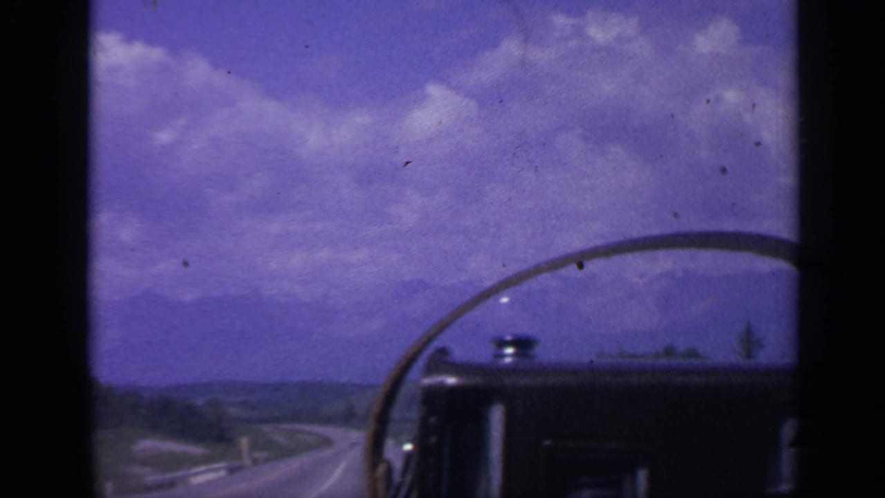 View through a vehicle windshield toward a winding road, hills, and a blue-purple sky.