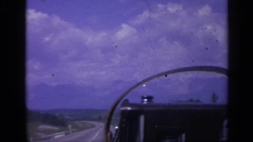 Colorado road-travel view from inside a moving vehicle, with windshield edge, open road, distant hills, and shifted color.