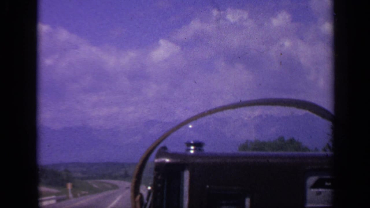 Road-trip footage through a vehicle windshield in Colorado, showing a curving road, open landscape, and distant hills.