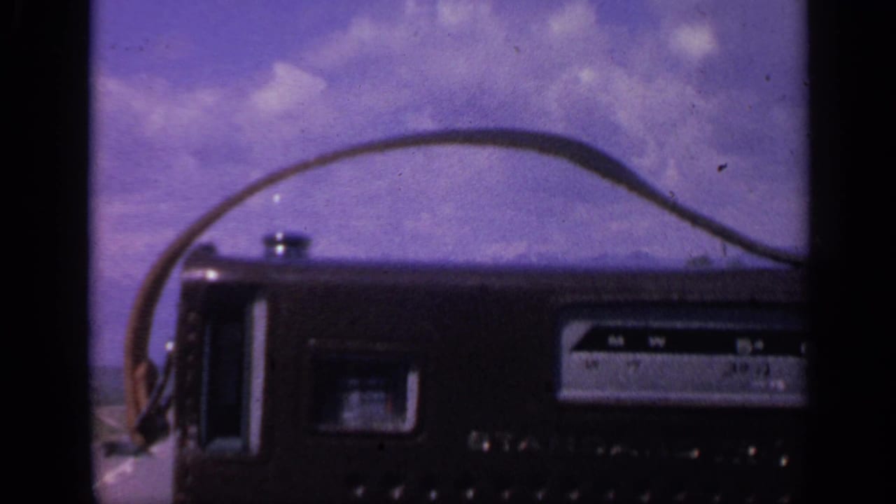 1959 Colorado 8mm frame from inside a moving automobile, showing dashboard, wiper, sky, clouds, and dark film borders.
