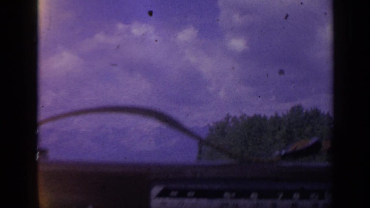 Interior automobile view in 1959 Colorado, with a wiper line across the sky and trees passing near the roadside.