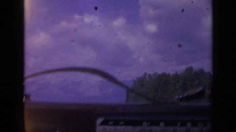 Interior automobile view in 1959 Colorado, with a wiper line across the sky and trees passing near the roadside.
