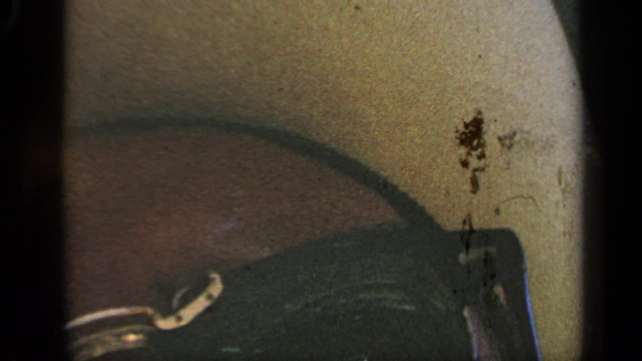 Close 8mm frame inside the car, showing a curved dark interior edge, pale windshield area, dust marks, and heavy film grain.