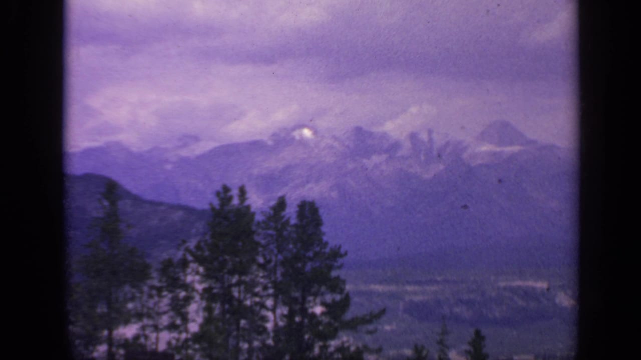 Colorado 8mm landscape frame with snow-capped peaks, layered ridges, evergreen foreground, and visible film borders.