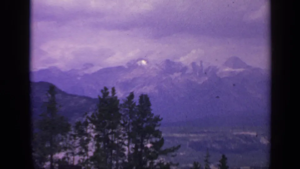 Colorado 8mm landscape frame with snow-capped peaks, layered ridges, evergreen foreground, and visible film borders.