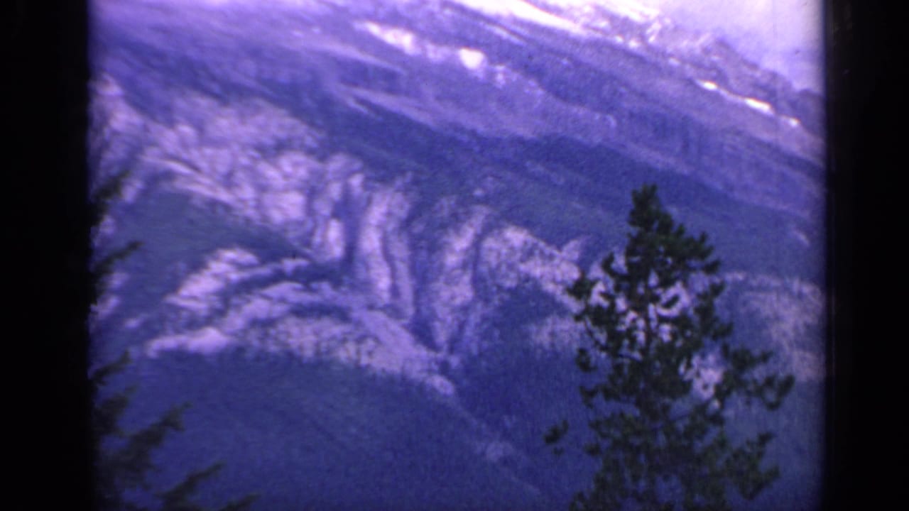 1959 Colorado 8mm frame showing a high view over a snow-streaked mountain gorge with pine silhouettes in front.