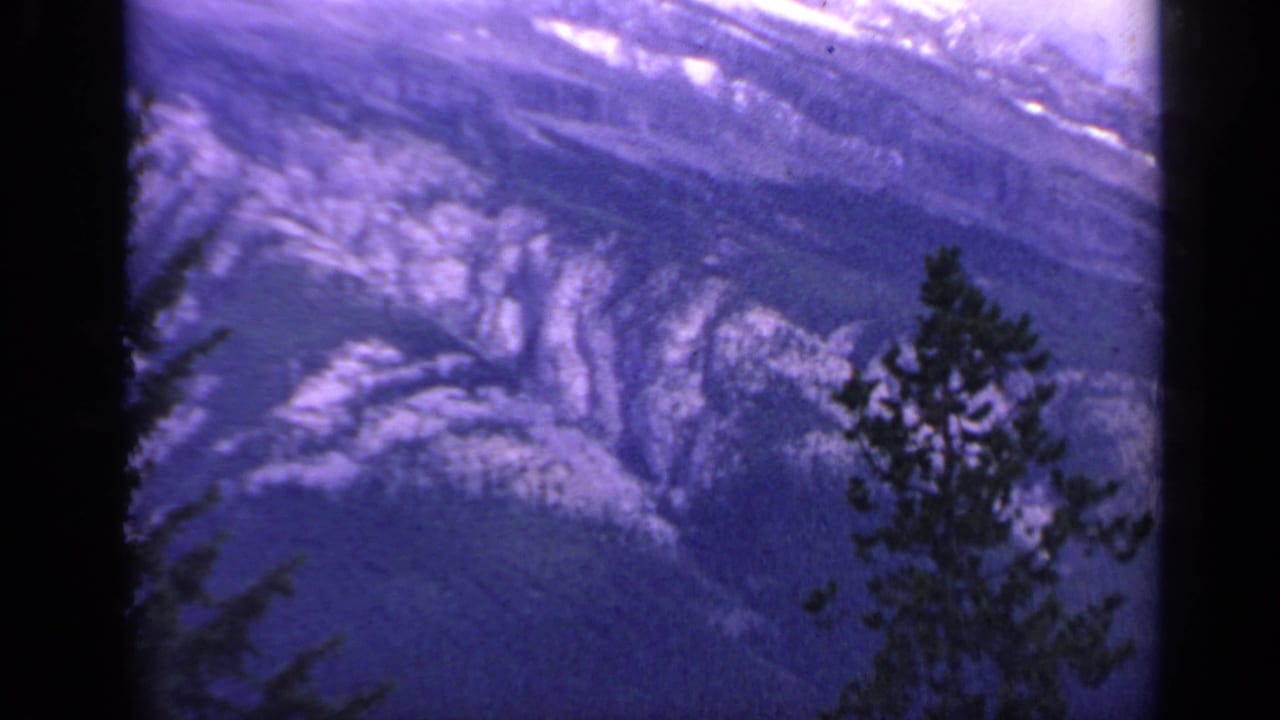 1959 Colorado 8mm frame showing a snow-marked mountain gorge with a dark pine silhouette near the lower right edge.