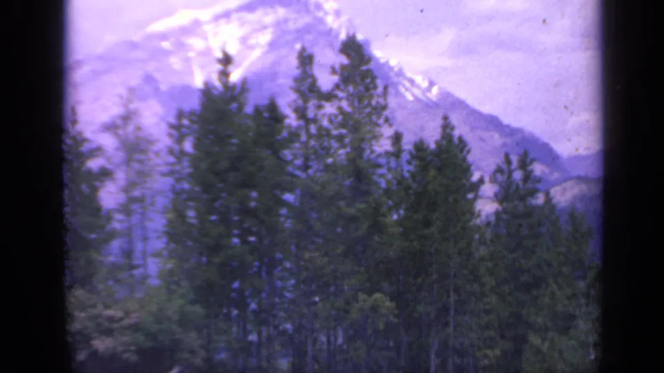 Distant Colorado mountain and forest captured on 8mm film, with soft focus, visible gate edges, and faded color.